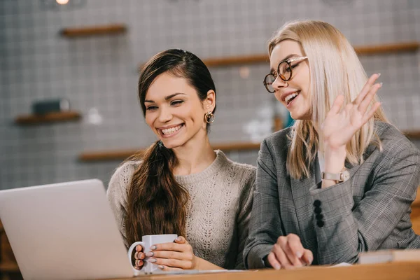 Mulher sorrindo olhando para laptop enquanto tem chamada de vídeo no café — Fotografia de Stock