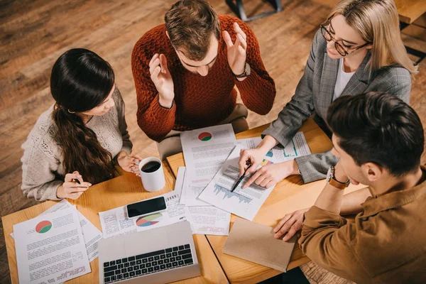 Overhead view of woman pointing at charts and graphs to coworkers in cafe — Stock Photo