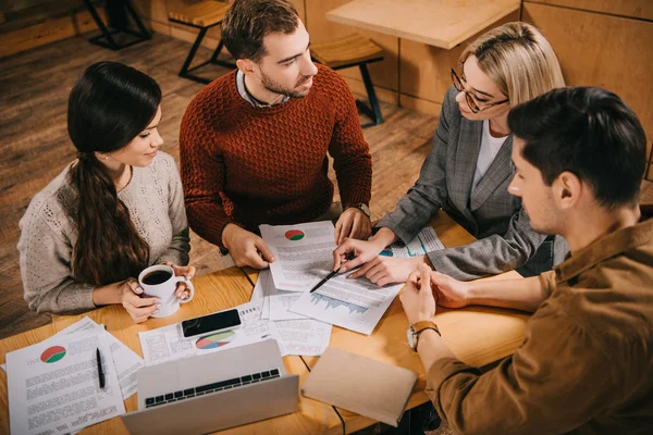 Woman pointing at charts and graphs to colleagues in cafe — Stock Photo