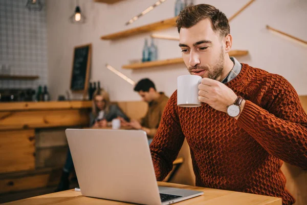 Schöner Mann trinkt Kaffee und schaut auf Laptop im Café — Stockfoto