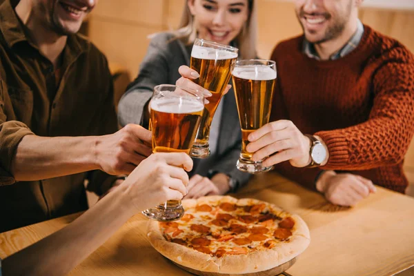 Vista ritagliata di amici clinking birra vicino pizza nel bar — Foto stock
