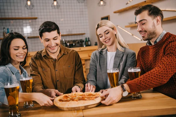 Cheerful friends smiling while taking pieces of tasty pizza in bar — Stock Photo