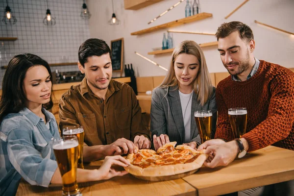Grupo de amigos sonriendo mientras toman trozos de sabrosa pizza en el bar - foto de stock