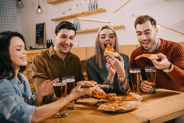 Happy woman eating pizza near friends in bar — Stock Photo