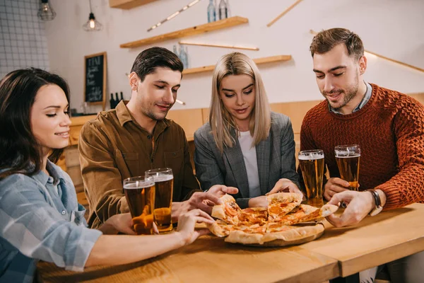 Amigos tomando trozos de sabrosa pizza en el bar - foto de stock