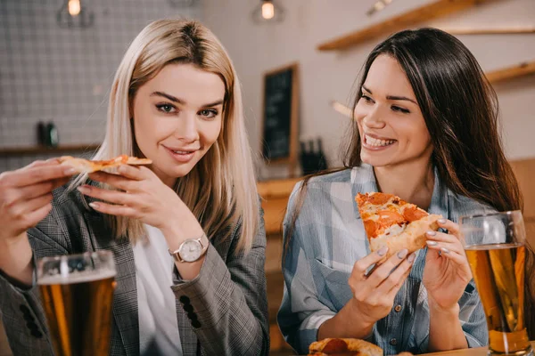 Cheerful friends holding pieces of tasty pizza in bar — Stock Photo