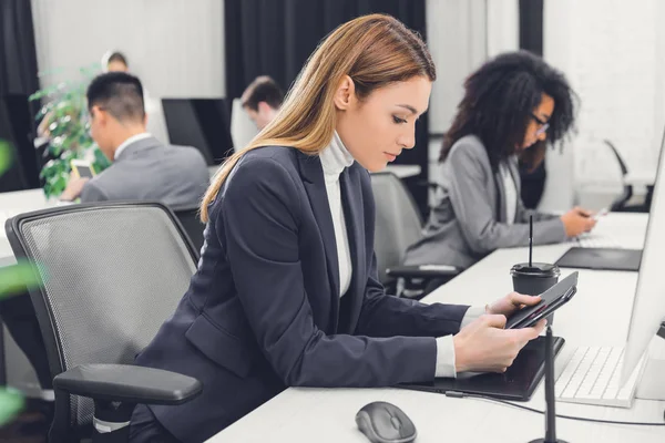 Vista lateral de la joven empresaria que utiliza dispositivos digitales en el lugar de trabajo - foto de stock