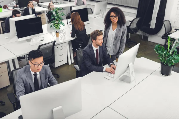 Vista de ángulo alto de los empresarios multirraciales que utilizan computadoras de escritorio en la oficina - foto de stock