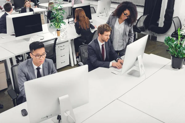 Vista de ángulo alto de los empresarios multiétnicos utilizando computadoras de escritorio en la oficina — Stock Photo