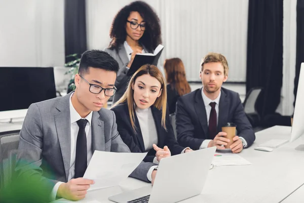 Professional young multiethnic business colleagues working with papers and laptop in office — Stock Photo