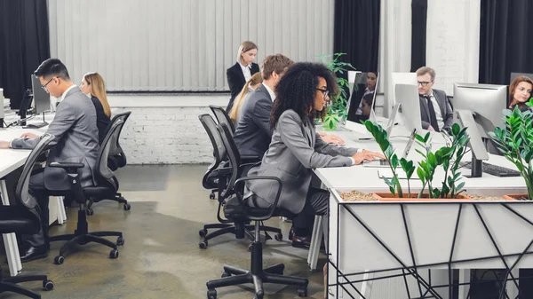 Seitenansicht professioneller multiethnischer junger Geschäftsleute, die mit digitalen Geräten im Großraumbüro arbeiten — Stockfoto