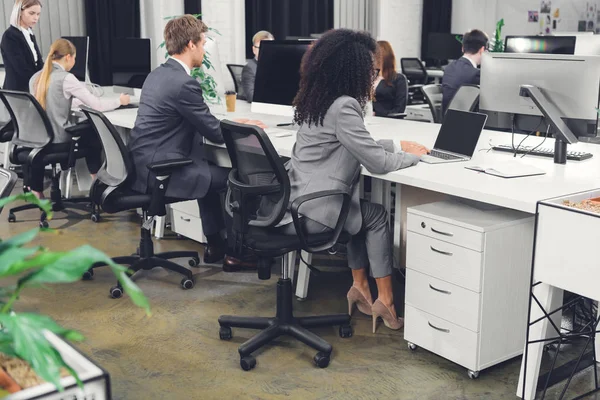Jovens empresários profissionais em vestuário formal que trabalham com dispositivos digitais em escritório de espaço aberto — Fotografia de Stock