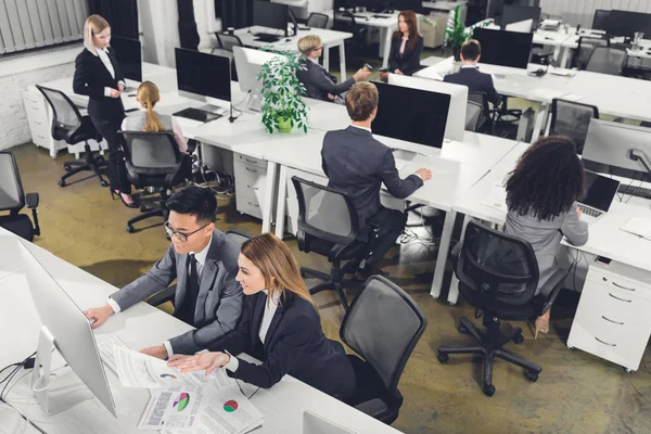 Hochauflösende Ansicht multiethnischer Geschäftsleute, die im Büro mit Papieren und Desktop-Computern arbeiten — Stockfoto