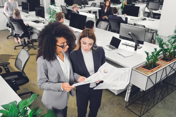 High angle view of young multiethnic businesswomen discussing papers with charts in office — Stock Photo