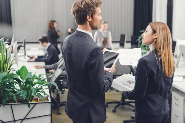 Back view of young businessman and businesswoman looking at each other while standing together in open space office — Stock Photo