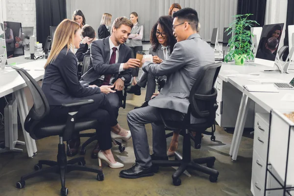 Sorrindo jovens empresários copos clinking enquanto sentados juntos durante coffee break no escritório — Fotografia de Stock