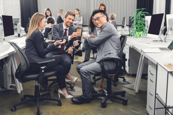 Smiling young businesspeople drinking coffee and talking during coffee break — Stock Photo