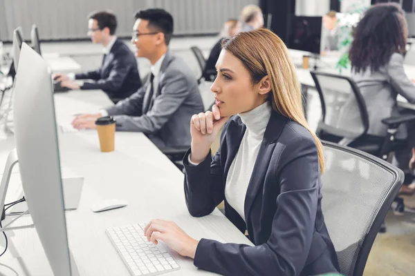 Konzentrierte junge Geschäftsfrau nutzt Desktop-Computer, während sie mit Kollegen im Großraumbüro arbeitet — Stockfoto