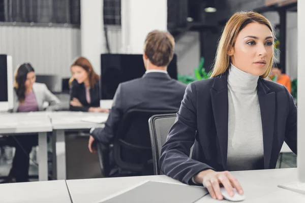 Bela focada jovem empresária sentado no local de trabalho e usando computador desktop — Fotografia de Stock