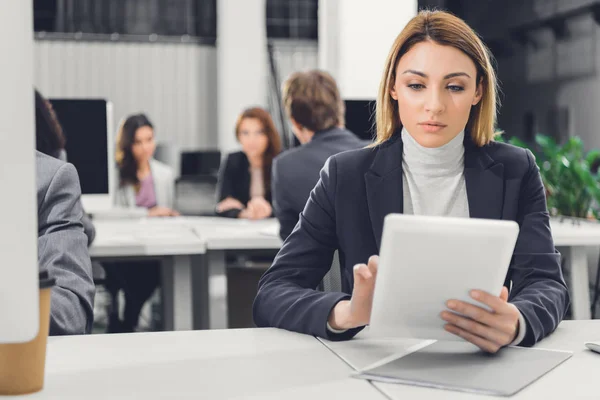 Fokussierte junge Geschäftsfrau nutzt digitales Tablet bei der Arbeit mit Kollegen im Großraumbüro — Stockfoto