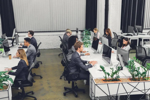Vista de ángulo alto de los jóvenes empresarios profesionales que trabajan con computadoras de escritorio en la oficina de espacio abierto - foto de stock
