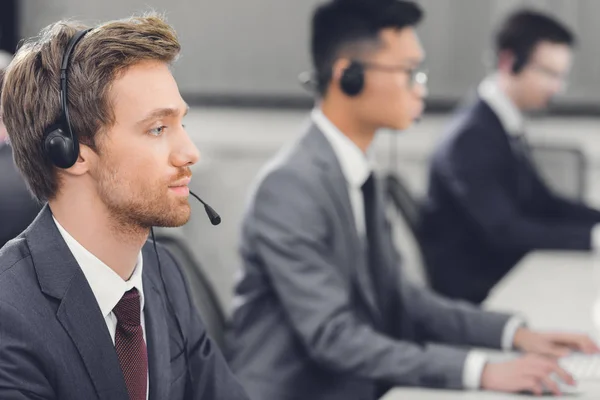 Vista lateral del joven empresario enfocado en auriculares que trabaja con colegas en el centro de llamadas - foto de stock