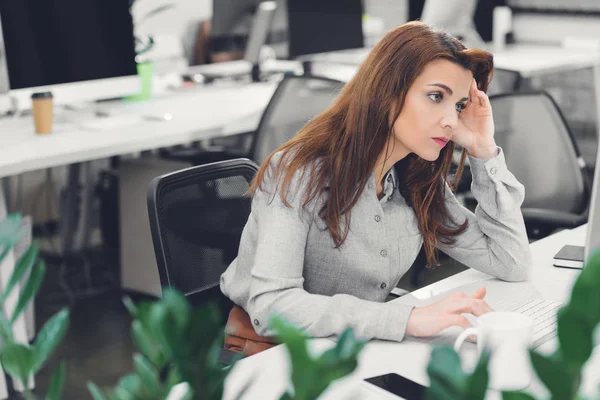 Tired young businesswoman using desktop computer at workplace — Stock Photo