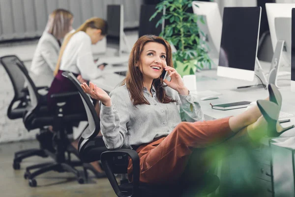 Happy young businesswoman talking by smartphone and looking up in open space office — Stock Photo