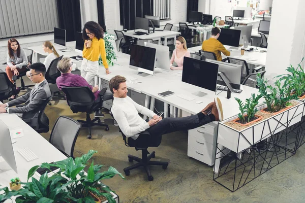 Vue en grand angle de jeunes collègues d'affaires parlant et travaillant dans un bureau à aire ouverte — Photo de stock
