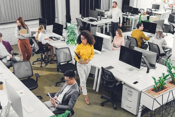 Blick aus der Vogelperspektive auf professionelle junge Geschäftsleute, die im Großraumbüro mit Computern und Dokumenten arbeiten — Stockfoto