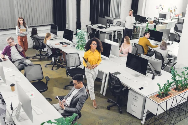 Vista ad alto angolo dei giovani imprenditori multirazziali che lavorano con computer e documenti in ufficio open space — Foto stock