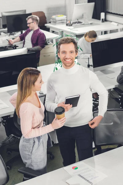 High angle view of happy businesswoman with coffee to go and smiling businessman standing together in office — Stock Photo
