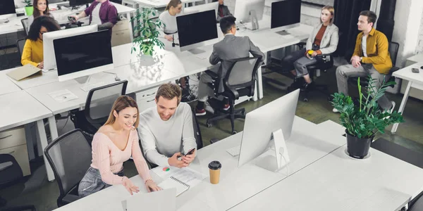 High angle view of smiling young businessman and businesswoman talking while working with colleagues in office — Stock Photo