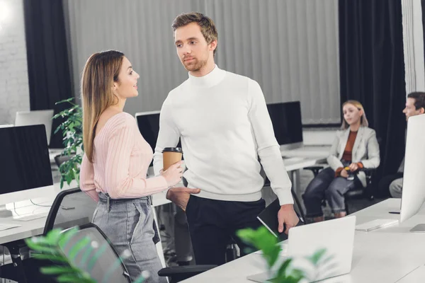 Handsome young businessman talking with attractive businesswoman holding coffee to go in office — Stock Photo