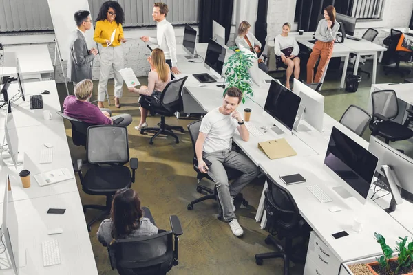 Vista de ángulo alto de los jóvenes empresarios profesionales que trabajan con papeles y computadoras en la oficina de espacio abierto - foto de stock