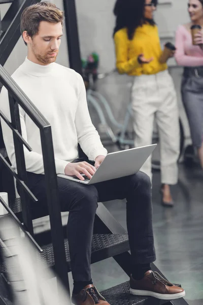 Focused young man sitting in staircase and using laptop in office — Stock Photo