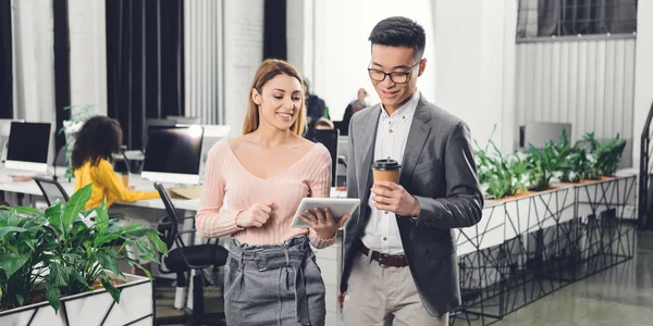 Heureux jeunes collègues d'affaires multiethniques utilisant une tablette numérique dans un bureau ouvert — Photo de stock