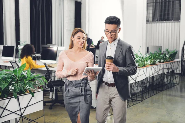 Collègues d'affaires souriants en utilisant une tablette numérique et marcher dans le bureau — Photo de stock