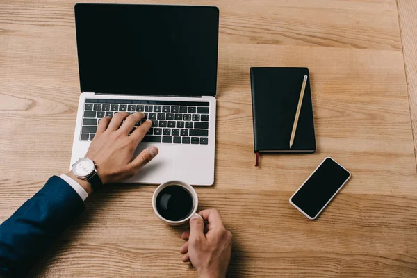 Abgeschnittene Ansicht eines Geschäftsmannes, der am Arbeitsplatz eine Tasse Kaffee auf seinem Laptop tippt — Stockfoto