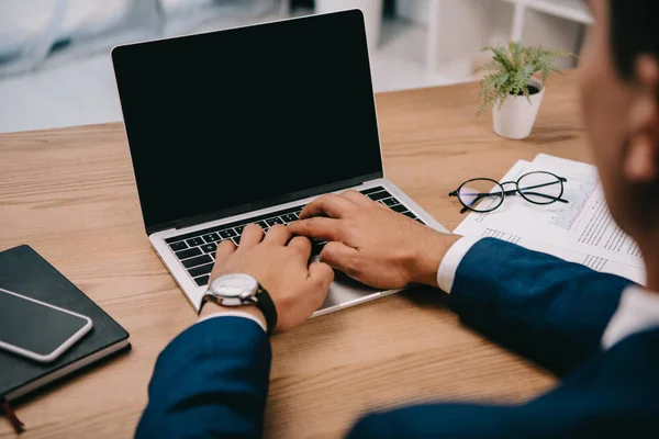 Vue recadrée de l'homme d'affaires tapant sur ordinateur portable sur le lieu de travail avec des documents — Photo de stock