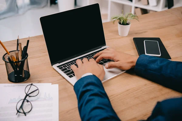 Vue recadrée de l'homme d'affaires tapant sur ordinateur portable sur le lieu de travail avec des documents et smartphone — Photo de stock