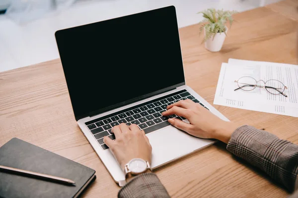 Ausgeschnittene Ansicht einer Geschäftsfrau, die am Arbeitsplatz mit Dokumenten am Laptop tippt — Stockfoto