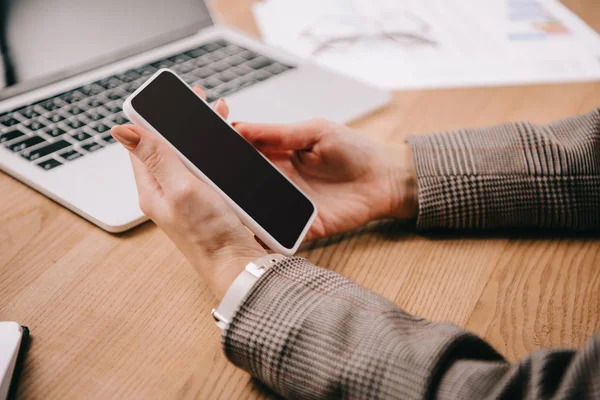 Cropped view of businesswoman using smartphone at workplace with laptop — Stock Photo