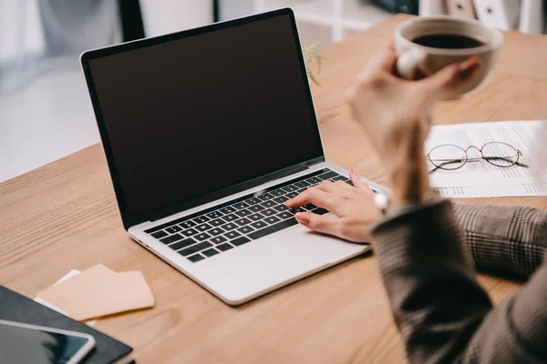 Abgeschnittene Ansicht einer Geschäftsfrau mit Kaffeetasse, die am Arbeitsplatz auf dem Laptop tippt — Stockfoto