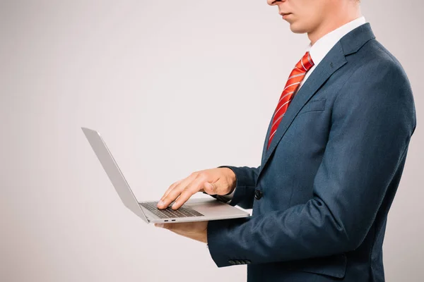 Vista recortada de hombre de negocios en traje usando portátil aislado en gris - foto de stock