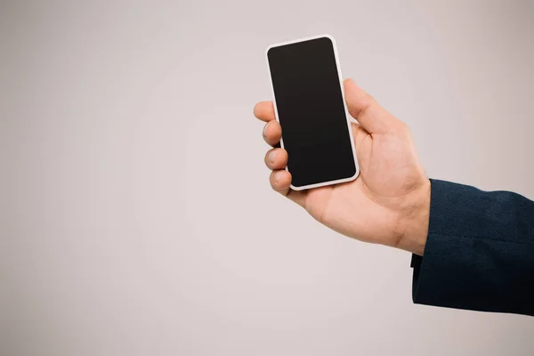 Vista recortada del empresario sosteniendo teléfono inteligente con pantalla en blanco aislado en gris - foto de stock