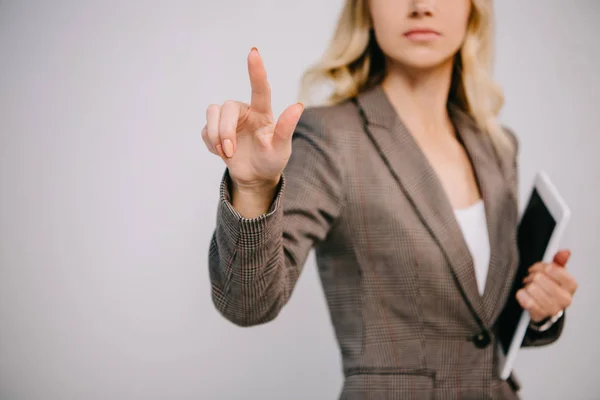 Vista recortada en mujer de negocios en traje sosteniendo tableta digital y apuntando aislado en gris - foto de stock