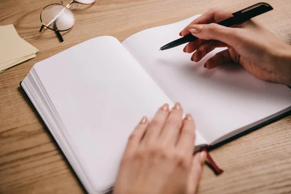 Visão recortada da mulher escrevendo em caderno no local de trabalho com óculos — Fotografia de Stock