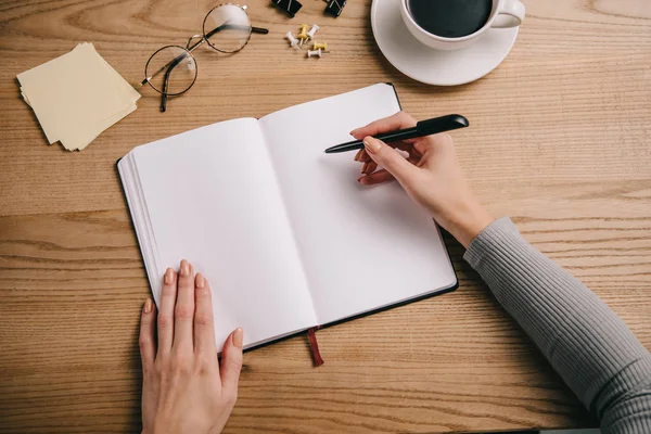 Vista cortada de empresária escrevendo em notebook no local de trabalho com copos e xícara de café — Fotografia de Stock