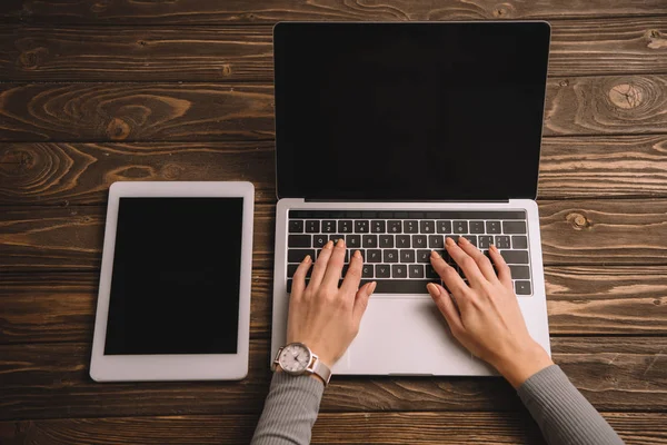 Vista recortada de la mujer escribiendo en el ordenador portátil en el lugar de trabajo con la tableta digital - foto de stock